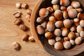 Whole hazelnuts in a wooden bowl on a wooden background.