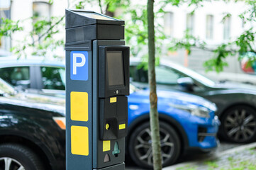A parking meter is positioned on the sidewalk, surrounded by parked cars and greenery, indicating an urban setting