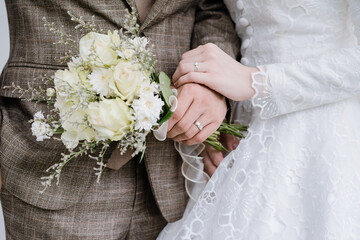 Close up Bride's hand wearing a wedding ring is holding the groom's hand wearing a wedding ring and holding a bouquet of white. Concept for wedding card background, poster, invitation card.