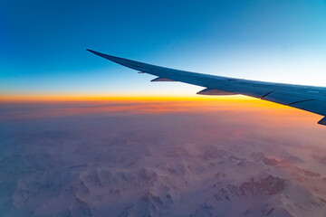 airplane wing above snow mountain in sunrise light