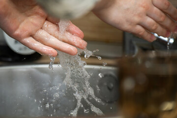 Teenager washing hands under running tap water in a kitchen sink, practicing hygiene and cleanliness