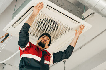 Technician installs ceiling air conditioning unit in modern office space during afternoon