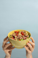 Woman holding bowl of delicious salad with canned tuna at blue background, top and front view. Space for text
