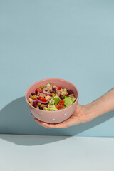 Woman holding bowl of delicious salad with canned tuna at blue background, top and front view. Space for text