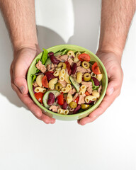 Man holding bowl of delicious salad with canned tuna at white table, top view. Space for text