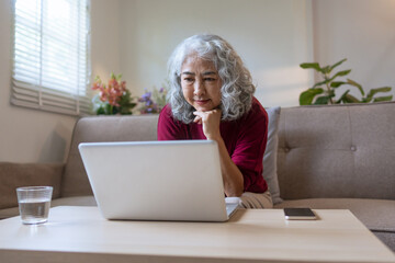 Senior woman enjoying time at home while shopping online with laptop and secure digital payment...