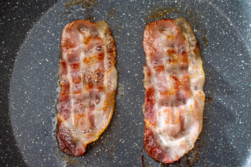 Currently, there are two slices of bacon being cooked in a frying pan