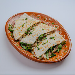Authentic Mexican quesadilla with melted cheese on a handmade clay plate, isolated on white background &ndash; traditional street food