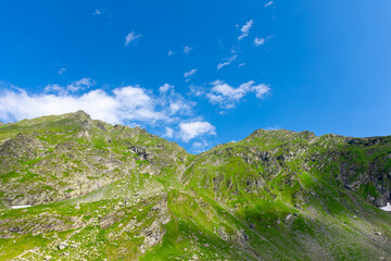 A mountain stands tall against a blue sky with fluffy clouds