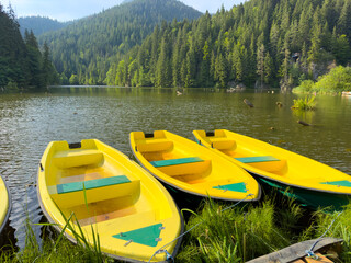 Three yellow boats float on a serene lake with mountains behind