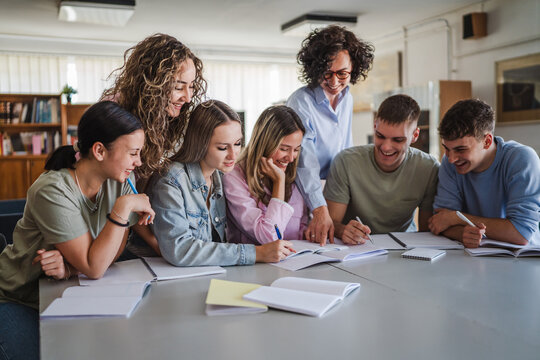 Group of high school students work on project with teacher in library