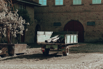 Rustic wooden cart waits in a quiet courtyard surrounded by historic stone buildings under soft...