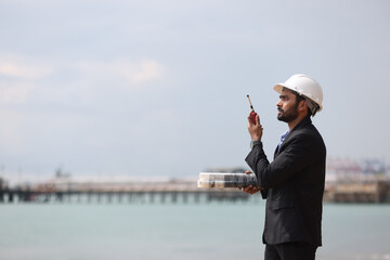 Business Man or Investor with black suit and safety hat working with drawing and digital tablet at front Refinery and gas petrochemical plant 