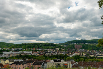 Lush green hills surround a charming town under a dramatic cloud-laden sky during a tranquil afternoon in spring