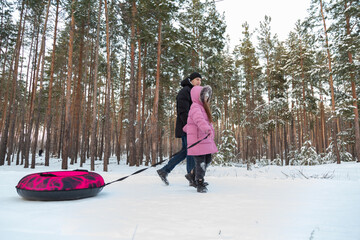 Dad with his daughter walking with snow tubing in the winter forest