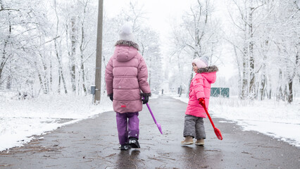 Two little girls in colorful clothes play outdoors during a snowfall.
