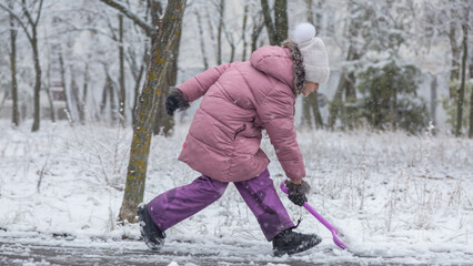 Little girl in colorful clothes play outdoors during a snowfall.