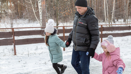 Little girls with her grandfather walking in park on snowy winter day
