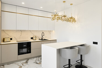 Modern kitchen with sleek white cabinetry, gold accents, marble backsplash, induction cooktop, and a striking chandelier. Includes bar stools and a minimalist design.