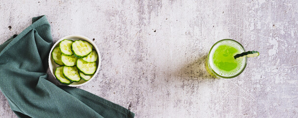 A glass of fresh cucumber juice and cucumbers on the table top view web banner