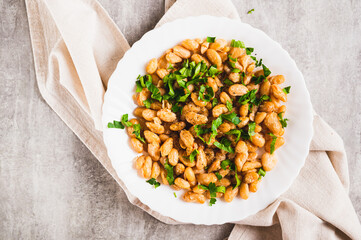 Close up of warm salad of white fried beans and parsley on a plate on the table top view