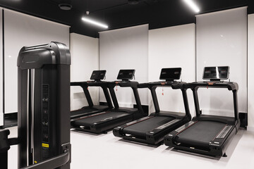Modern gym with sleek black treadmills featuring digital displays, ergonomic designs, and safety features. Minimalist white walls and bright lighting create a clean, focused workout environment.
