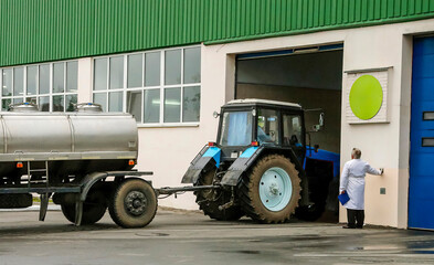 Tractor unloading milk from tanker outside dairy processing facility in early morning hours