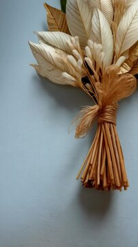 Arrangement of elegant dried leaf and flower bouquet with golden accents tied with raffia on a soft blue surface