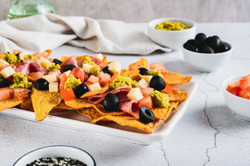 Mexican nachos chips with olives, tomatoes, salami and cheese on a plate on the table