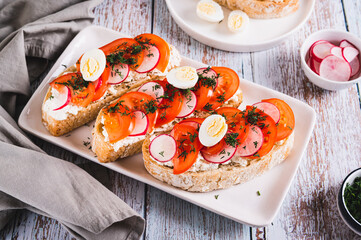 Sandwiches with ricotta, tomato, radish and egg on a plate on a table