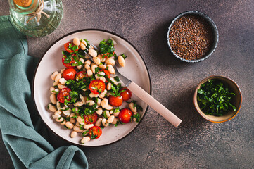 Appetizing salad of white beans, cherry tomatoes and parsley on a plate top view