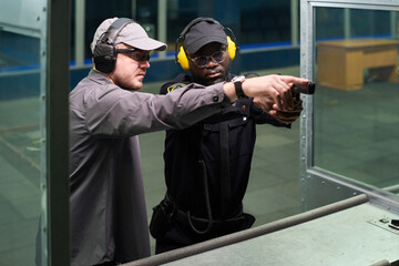 Gun instructor giving shooting lessons at indoor gun range, displaying correct shooting stance and...