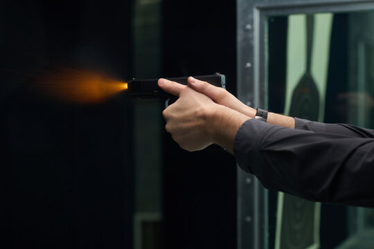 Hands of person gripping firearm while firing at indoor shooting range, showcasing firearm handling and aim practice in controlled environment