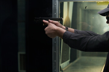 Person seen firing a handgun at indoor shooting range during practice session, focused on the hands and gun. Visible target in background within shooting lane
