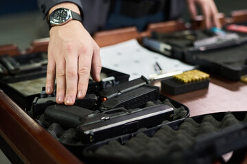 Close-up of person inspecting firearms displayed in a storage facility, with various guns and ammunition arranged in organized fashion