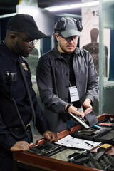 Instructor showing student how to properly handle a handgun at an indoor shooting range. Both...