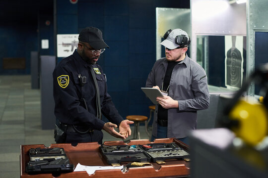 Two security professionals in discussion while inspecting security gear on desk Two men in uniform examining equipment in well-lit office space