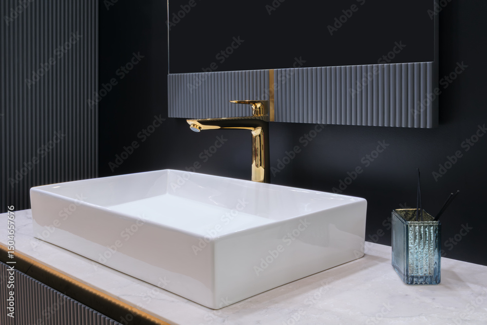 Poster a white bathroom sink with a gold faucet sits in front of a mirror. the sink is rectangular and has 