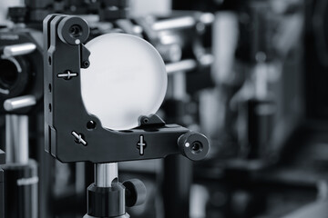 Optical equipment including telescope and lenses are displayed on a table in a laboratory. Optics and photonics concept science experiment with laser background