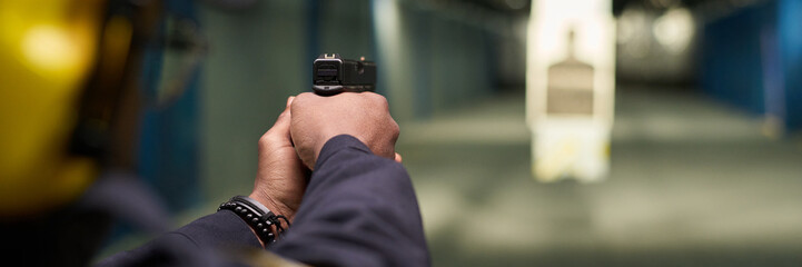 Person holding and aiming handgun while practicing target shooting at indoor range. Emphasis on...
