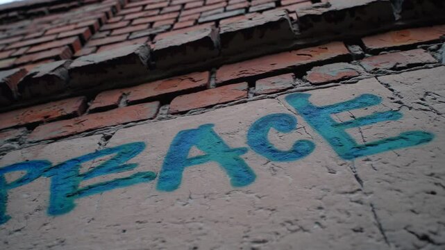 Peace graffiti in blue letters on cracked wall with exposed bricks

