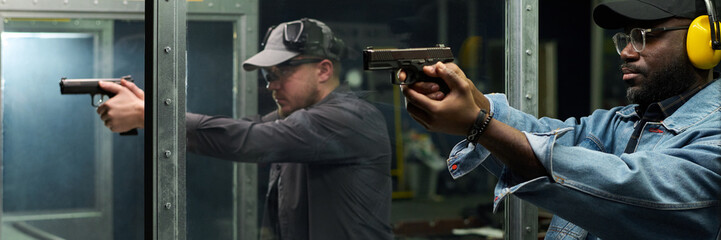 Two individuals focusing on their target at indoor gun range, showing concentration and precision...