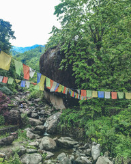 Colourful prayer flags around a rocky forest covered water stream in the hills of Kalimpong, West Bengal, India in May 2024....