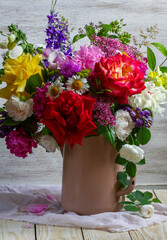 A bouquet of different flowers, roses, peonies, lupines, daisies, dilphinium, snapdragon and others in an old teapot.
