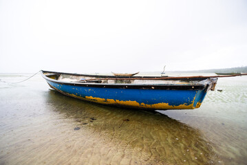 Fototapeta premium Fishing boat anchored on the sand of a dry beach. Quite rainy day with dense clouds.