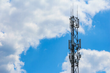Cell tower with multiple directional antennas photographed from low angle against cloudy blue sky