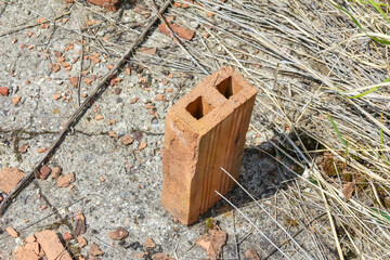 A single red brick stands upright on a concrete slab, surrounded by broken brick fragments and dirt, symbolizing a remnant of former construction,