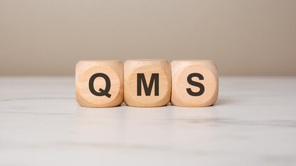 Wooden cubes with QMS acronym on marble surface, quality management concept.