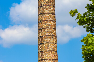 Red brick industrial chimney photographed from low angle against dramatic blue sky with white clouds