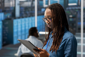 Engineer in server room using tablet to implement and manage data backup solutions to protect against data loss and ensuring efficient recovery processes, identifying and resolving technical issues